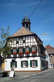 Das Bild zeigt das Alsheimer Rathaus. Das Gebäude ist ein Fachwerkhaus mit kleinem Turm, das direkt an einer Straßenrkeuzung im Ortskern von Alsheim liegt.
