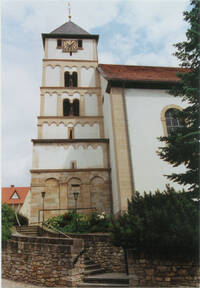 Das Bild zeigt die romanische Kirche in Albig. An das Kirchenhauptgebäude ist ein Wehrturm mit Uhrwerk angefügt.