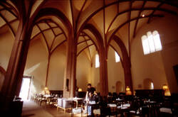 Das Bild zeigt den großen Innenraum des Heilig-Geist-Spitals mit dem gotischen Gewölbe. Im unteren Teil sind Tische sowie Gäste und ein Kellner des Gastronomiebetriebes zu sehen.