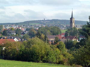 Blick auf Waldalgesheim und den Ortsteil Genheim. Rechts der Kirchturm der evangelischen Kirche Genheim, dahinter der Turm der katholischen Kirche Waldalgesheim. Auf dem Hügel im Hintergrund die Grube Amalienhöhe/Dr. Geier mit dem 2014 abgerissenen Förderturm.