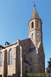 Das Foto zeigt die neugotische Kirche St. Maria Magdalena von Außen. Zu sehen ist die Front und der Turm mit dem Spitzdach.