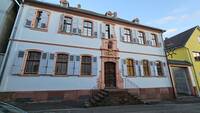 Das katholische Pfarrhaus in der Herrnsheimer Hauptstraße 18 ist ein zweigeschossiger barocker Putzbau mit Walmdach und geschmückter Fassade.