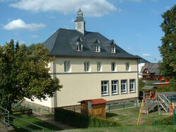 Auf dem Foto ist die "Alte Schule" in Werlau zu sehen: ein hellgestrichenes zweistöckiges Gebäude, dessen Erdgeschoss sehr hoch ausgefallen ist. Das Dach besitzt Dachgauben und ein kleines Türmchen.