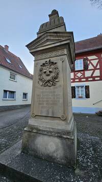 Auf dem kleinen Platz vor der Gasthaus "Zum Löwen" befindet sich das Herrnsheimer Kriegerdenkmal für die Teilnehmer des Deutsch-Französischen Krieges 1870/71. Das Denkmal besteht aus einer Sandsteinstele mit giebelartigem Kapitel und kuppelartigem Aufsatz. Auf der Frontseite befindet sich eine Widmung der Gemeinde Herrnsheim und auf den anderen drei Seiten sind die Namen der Soldaten aus Herrnsheim gelistet.