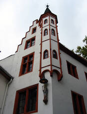 Spätgotisches Patrizierhaus mit weißem Verputz und roten Sandsteinfenster. In der Mitte des Bildes sieht man den Erkerturm, darunter eine Madonna. Über dem Erkerturm erhebt sich der Treppengiebel. Das Foto ist aus starker Untersicht aufgenommen.